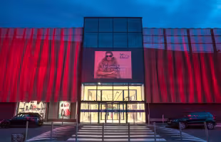 Centre Commercial La Valentine, entrée vitrée sous une façade rouge, parvis en passage piéton