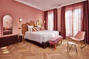 Hôtel de Cambis, chambre aux murs roses avec parquet en chevrons, lit blanc et rideaux bordeaux