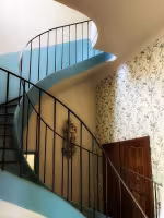 Bastide Craponne, escalier en colimaçon à rampe métallique, mur tapissé de papier peint à motifs végétaux
