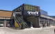 Centre Commercial Grand V, façade d'entrée avec escalators sous l'enseigne, parement en bois et en brique