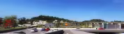 Centre Commercial La Valentine (ESQ), perspective depuis le parking avec kiosques commerciaux à toit végétalisévec panneaux solaires sous un ciel dégagé